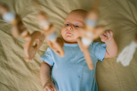 Newborn baby observing a wooden mobile, stimulating interest and cognitive development, reflecting on childhood wonder and developmental stages in a calming sleep environment