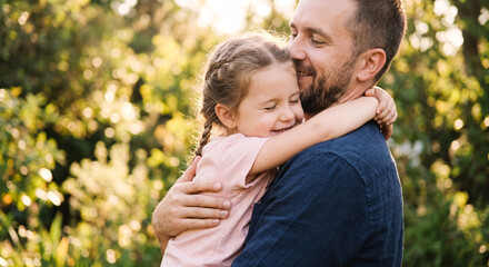 Fototapeta premium Happy young father hugging his little daughter outdoors in summer park.