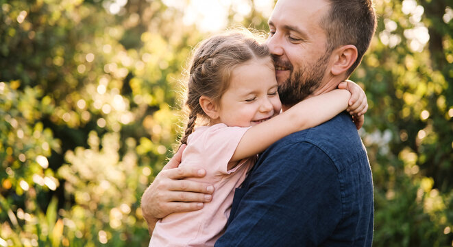 Happy young father hugging his little daughter outdoors in summer park.