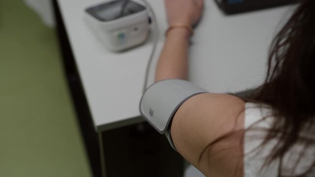 A close up of a woman measuring her blood pressure with an electronic cuff at home or in a clinic. Useful for healthcare, wellness, and medical technology themes.