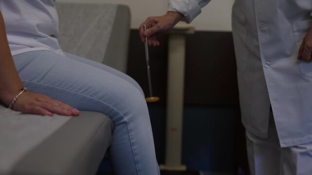 A healthcare professional performs a neurological reflex test on a patients knee using a medical mallet. Authentic clinical procedure for wellness and diagnostic checkups.
