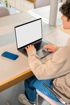 Man using laptop with white screen in office alongside smartphone