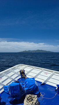 View of the bow of a boat with blue covers and coiled rope, looking out towards the distant island of Ko Tao under a clear blue sky in Ko Tao, Surat Thani, Thailand.