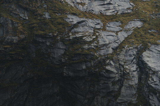View of the rugged, dark, rocky cliff face of Lofoten with patches of green moss and textured stone surfaces, Nordland, Norway.