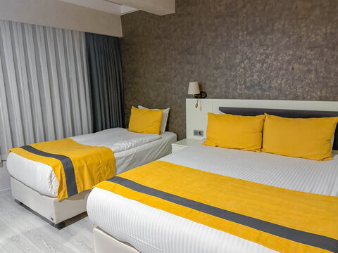 Modern hotel room featuring double bed, single bed, yellow pillows, matching bed runners, stylish interior, cozy accommodation for family travel, vacation, hospitality, comfort concept