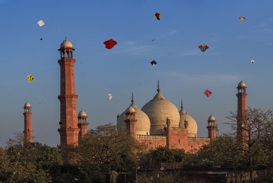 View of the historic Badshahi Mosque with numerous colorful kites flying in the blue sky during the Basant festival in Lahore, Punjab, Pakistan.