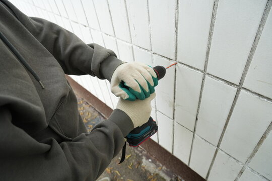 Worker using teal cordless drill on building facade wall
