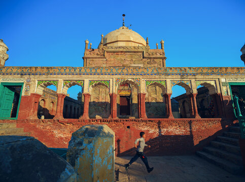 View of the historic Tomb of Shah Burhan with a young boy running past the intricate arches and decorative masonry in Chiniot, Punjab, Pakistan.
