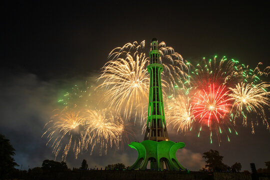 View of the illuminated Minar-e-Pakistan monument surrounded by vibrant fireworks in the night sky in Lahore, Punjab, Pakistan.