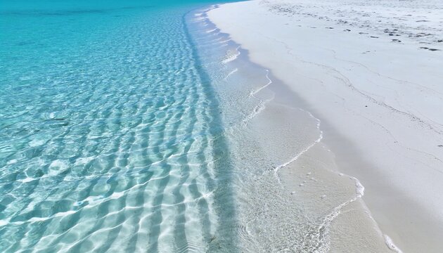 Showing shoreline where clear aqua water forming ripples, lapping white sand with seaweed tracks