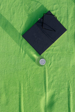Top view of green beach towel with book sunglasses and water bottle