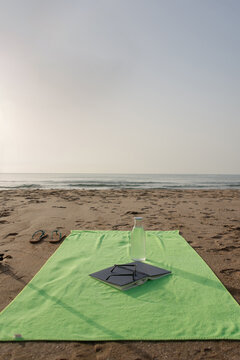 Green beach towel with book sunglasses water bottle and flip flops