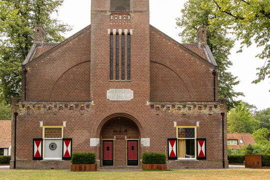 View of De Brandtoren, a historic brick building with distinctive red and white shutters and arched entrance, located in Esbeek, Noord-Brabant, Netherlands.