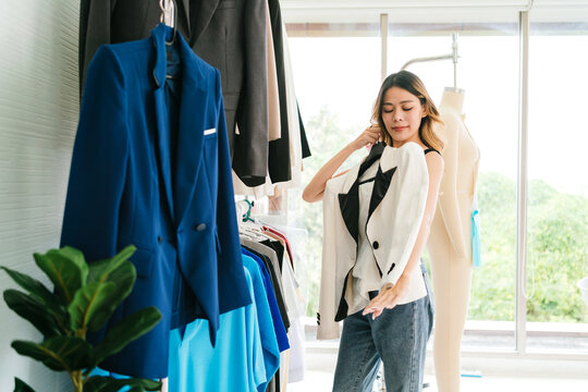 A woman selects a blazer in a bright home studio, surrounded by hanging jackets and a mannequin.