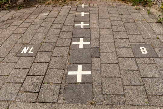 View of the international border line marked with white crosses on stone pavement separating the Netherlands and Belgium in Baarle-Nassau, North Brabant, Netherlands.