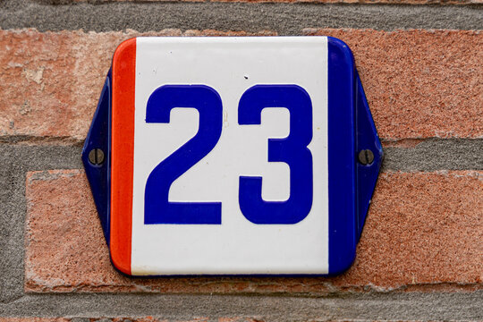 View of a house number sign with the number 23 mounted on a brick wall in Baarle-Nassau, North Brabant, Netherlands.