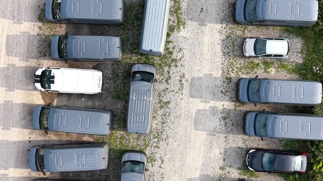 Aerial view of multiple new minibuses parked in a row on a gravel lot, showcasing their sleek design and uniform color against the natural landscape and shadows. Industrial place