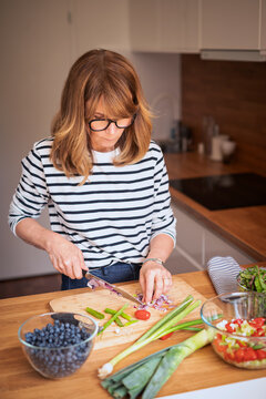 Mid-aged woman chopping fresh vegetables on a wooden cutting board in a modern kitchen