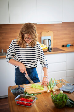 Mid-aged woman chopping fresh vegetables on a wooden cutting board in a modern kitchen