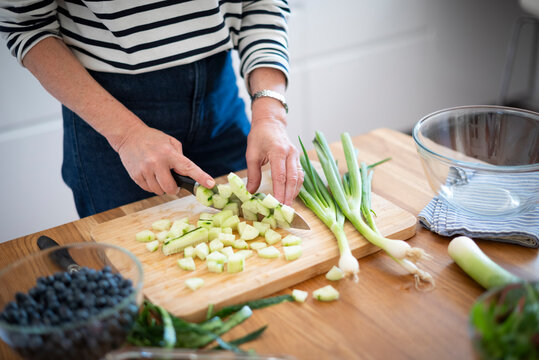 Mid-aged woman chopping fresh vegetables on a wooden cutting board in a modern kitchen