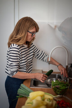 Blond haired mid-aged woman washing a cucumber in a modern kitchen sink