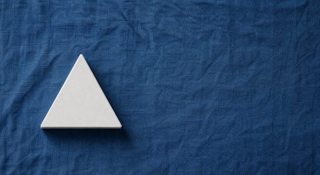 equilateral. Single white equilateral triangle object on deep blue linen, calm still life for editorial concept, lifestyle magazines.