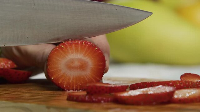 Extra close up, slow motion shot of knife slicing through juicy strawberry
