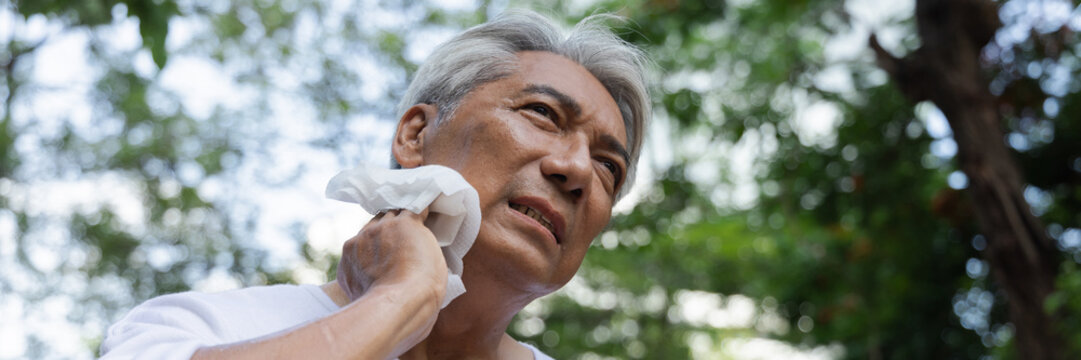 Nervous, restless, unpleasant elderly asian senior man wiping his face with high quality refreshing cold wet towel to cool himself down in the very hot summer