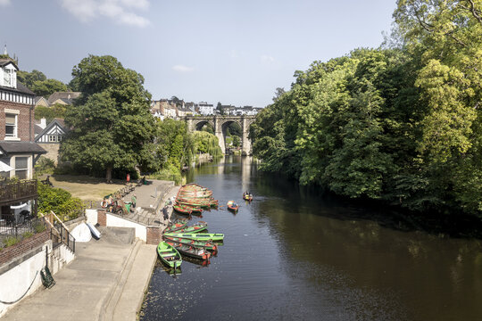 View of the River Nidd with colorful rowboats moored at the bank and the historic railway viaduct in the background in Knaresborough, England, United Kingdom.