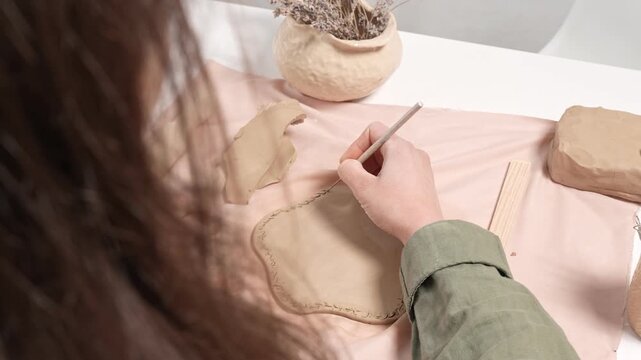 Artisan Carving Clay Texture with Tool 4K Video. Artist uses a sharp metal carving tool to incise a repeating decorative texture into the curved wall of a clay artwork