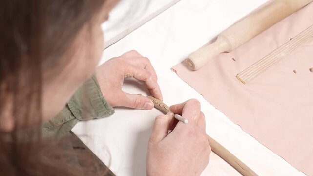 Artisan Carving Clay Texture with Tool 4K Video. Artist uses a sharp metal carving tool to incise a repeating decorative texture into the curved wall of a clay artwork