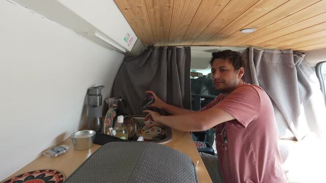 Timelapse of young man washing dishes inside camper van kitchen embracing van life and nomadic style