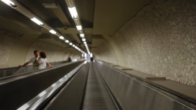 Underground tube corridor in soft defocused bokeh with long escalator and textured stone wall, station; background, backplate, copyspace, calm.