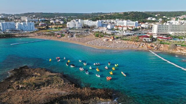 Drone view of Fig Tree Beach and Protaras coastline in Cyprus. Turquoise water, small boats, sandy beach and resort buildings shape a bright summer panorama.
