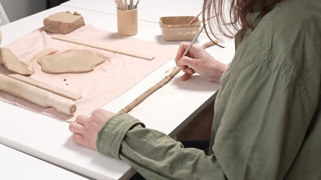 Artisan Carving Clay Texture with Tool 4K Video. Artist uses a sharp metal carving tool to incise a repeating decorative texture into the curved wall of a clay artwork