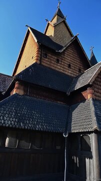 Upward view of ornate timber church rooflines and gables in Norway, lit by warm sunlight on a clear day.