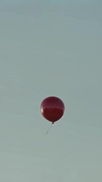 Red balloon rising slowly into wide pale sky