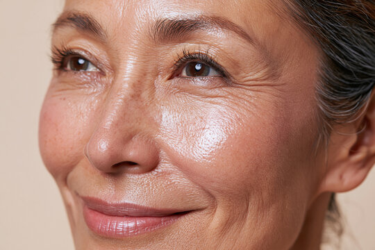 Radiant middle aged Asian woman close up with natural skin texture, freckles, fine lines and gentle smile conveying confidence and warmth