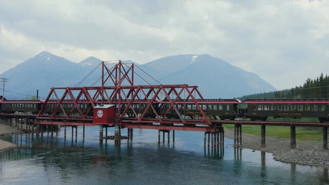 Historic White Pass and Yukon Route train traveling over railway bridge with mountains background in Carcross, Canada