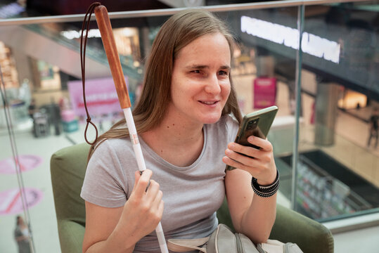 Visually impaired woman with white cane using smartphone app in shopping mall