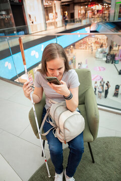 Visually impaired woman with white cane using smartphone app in shopping mall