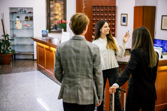 Hotel employee explaining details to business couple from behind in luxury lobby