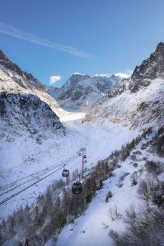 View of the snowy Mer de Glace glacier and the Montenvers cable car system surrounded by dramatic alpine peaks under a clear blue sky in Chamonix, Auvergne-Rhone-Alpes, France.