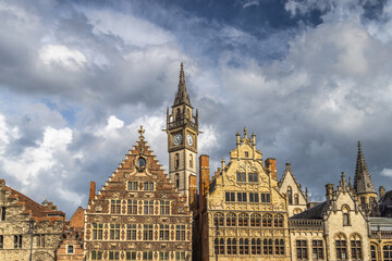 Obraz premium Ghent town in Belgium, Europe. Historic European Architecture Under Dramatic Sky: A Collection of Ornate Gabled Buildings and a Prominent Clock Tower