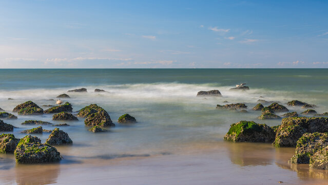 Tranquil Coastal Scene with Moss-Covered Rocks and Serene Sea Water Under a Clear Blue Sky at Sunset or Sunrise Time. Ostend, a coastal city in Belgium, Europe.