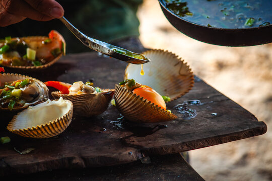 View of freshly cooked shellfish being seasoned with herbs on a wooden board on the beach in Phu Quoc, Kien Giang, Vietnam.