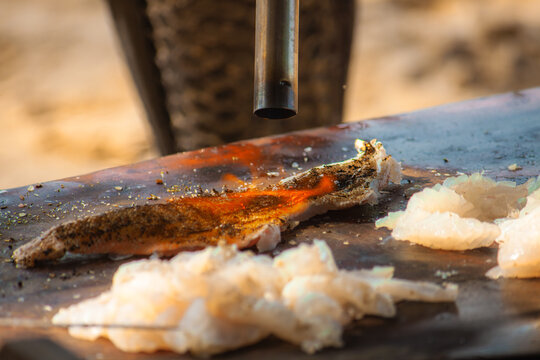 View of a blowtorch searing a piece of fresh fish on a wooden board with raw seafood pieces nearby on Phu Quoc, Kien Giang, Vietnam.