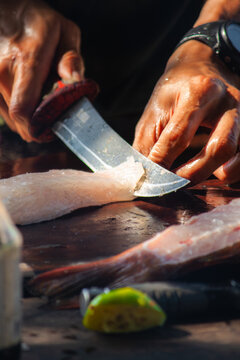 View of a person using a sharp knife to fillet fresh fish on a wooden cutting board on the beach in Phu Quoc, Kien Giang, Vietnam.