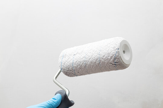 Hand in blue glove holding paint roller against white wall