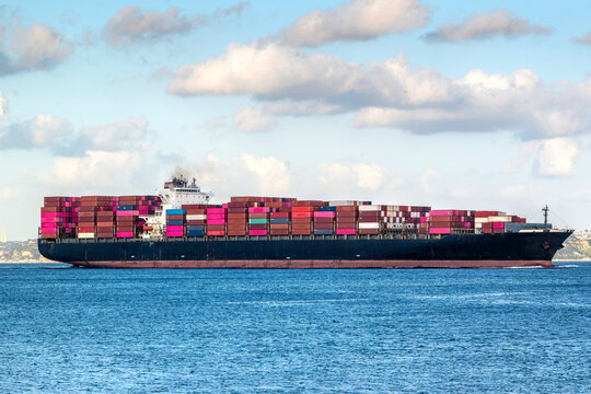 View of a large cargo vessel loaded with colorful shipping containers sailing on the blue sea near the coast of Carcavelos, Lisbon, Portugal.